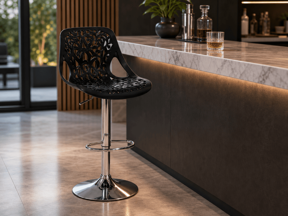 A modern black perforated plastic bar stool with a chrome pedestal base, positioned in front of a contemporary kitchen island with a marble countertop.