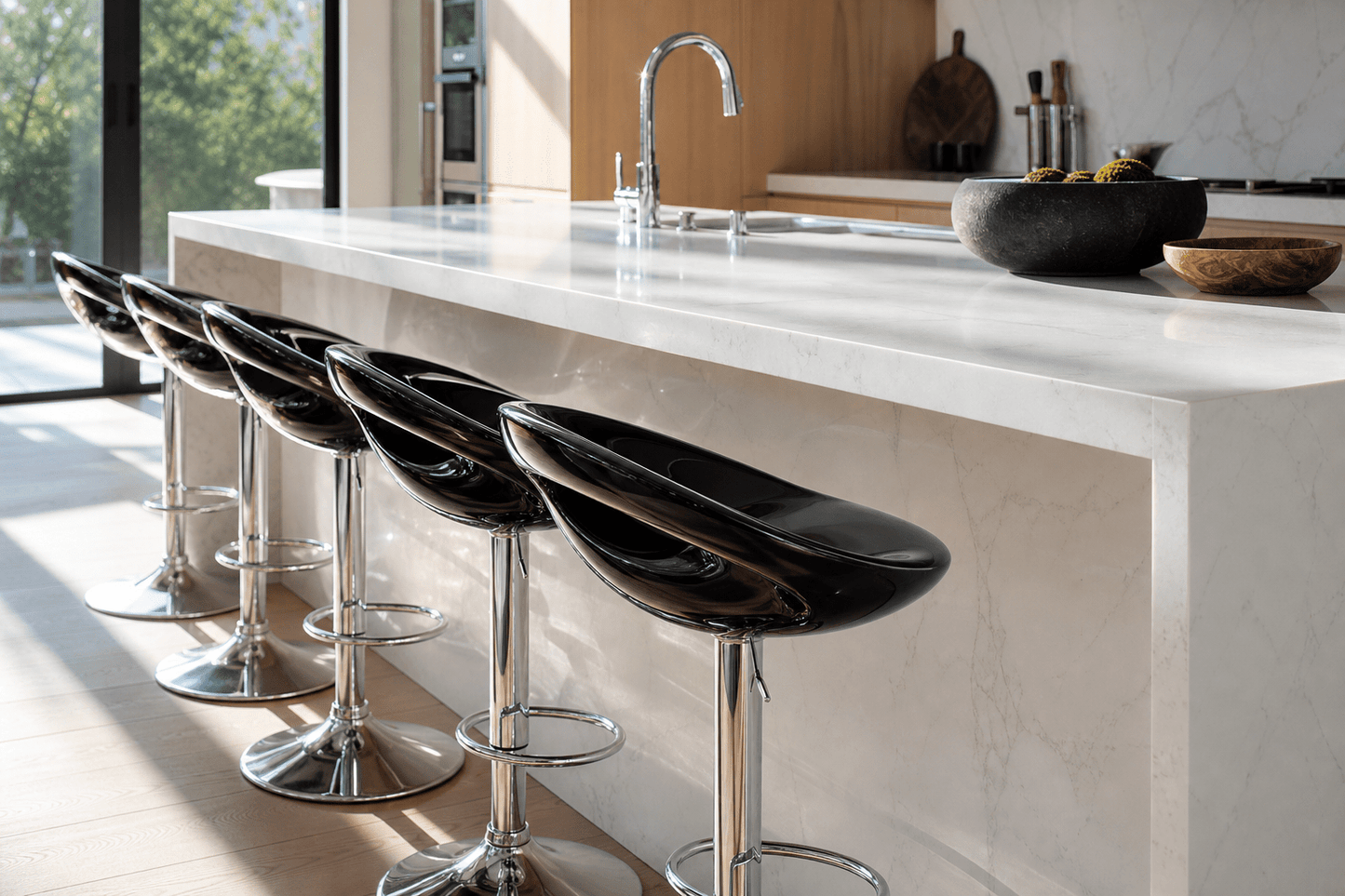 Five glossy black bar stools with chrome pedestal bases lined up along a white marble kitchen island in a modern kitchen setting.