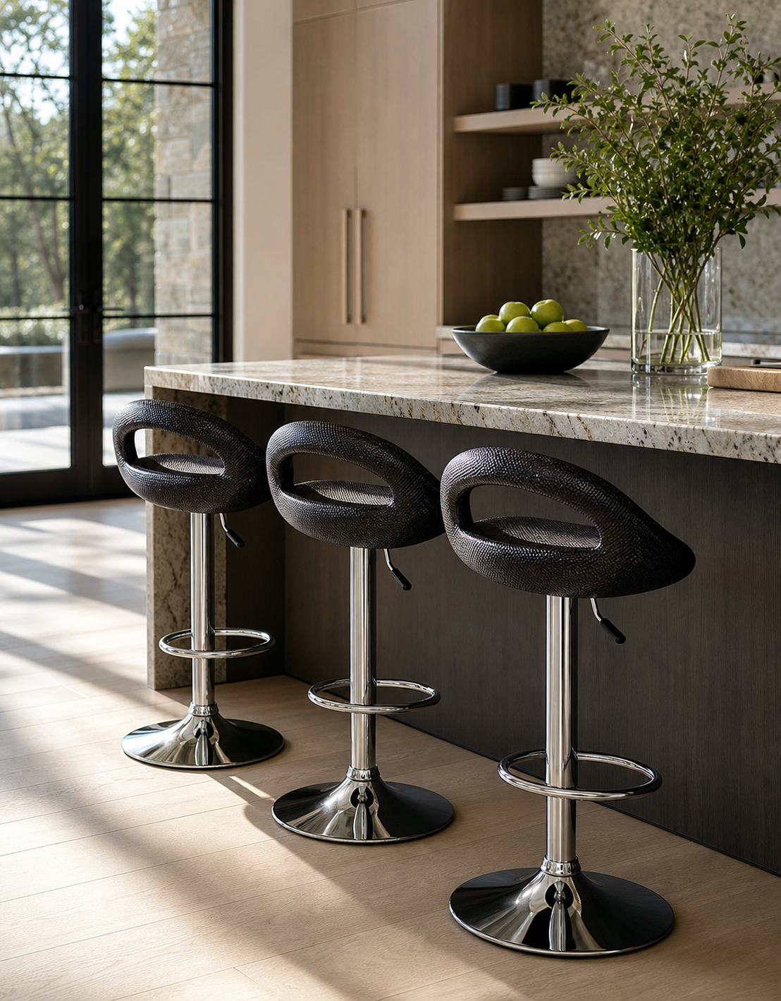 Three modern swivel bar stools with textured black seats and polished chrome bases arranged along a kitchen island with a marble countertop in a bright interior.