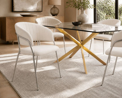 A modern dining room scene featuring a glass-top table with a yellow wooden X-shaped base, surrounded by white upholstered chairs with chrome legs, set on a light rug in a bright interior.