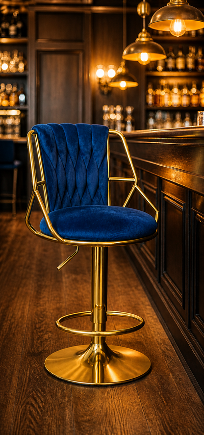 A luxury bar stool with a deep blue velvet tufted seat and backrest, supported by a polished gold-finished metal frame and swivel base, set in a dimly lit, warm bar environment.