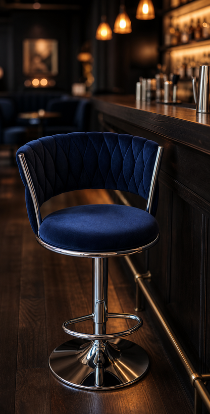 A dark blue velvet swivel bar stool with a chrome metal base, positioned in a dimly lit bar environment with wooden floors and a bar counter in the background.