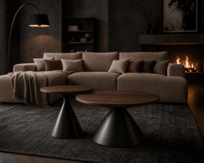 A modern living room scene featuring a beige corduroy sectional sofa with matching pillows, two round nesting coffee tables with dark wood tops and black metal bases, a dark textured rug, a black floor lamp, and a lit fireplace in the background.