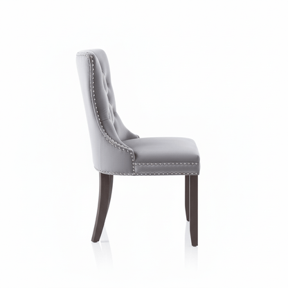 Side view of a grey upholstered dining chair with stud trim on a white background That Couch Place