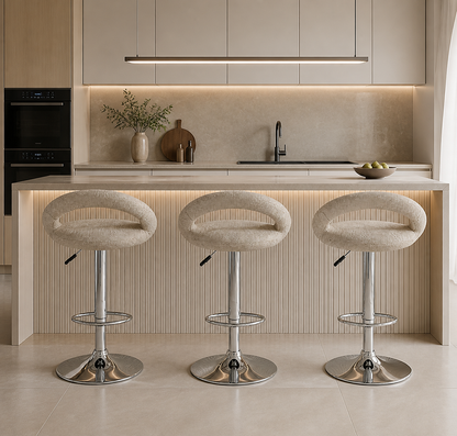Three modern swivel bar stools with cream bouclé seats and chrome pedestal bases, arranged in front of a light wood kitchen island with warm under-cabinet lighting.