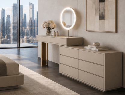 A modern beige bedroom furniture set featuring a long vanity table with a built-in illuminated oval mirror and a matching six-drawer dresser, styled in a luxury loft with a city skyline view.