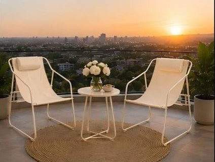 Two beige chairs with a small round table on a balcony with a cityscape view during sunset.