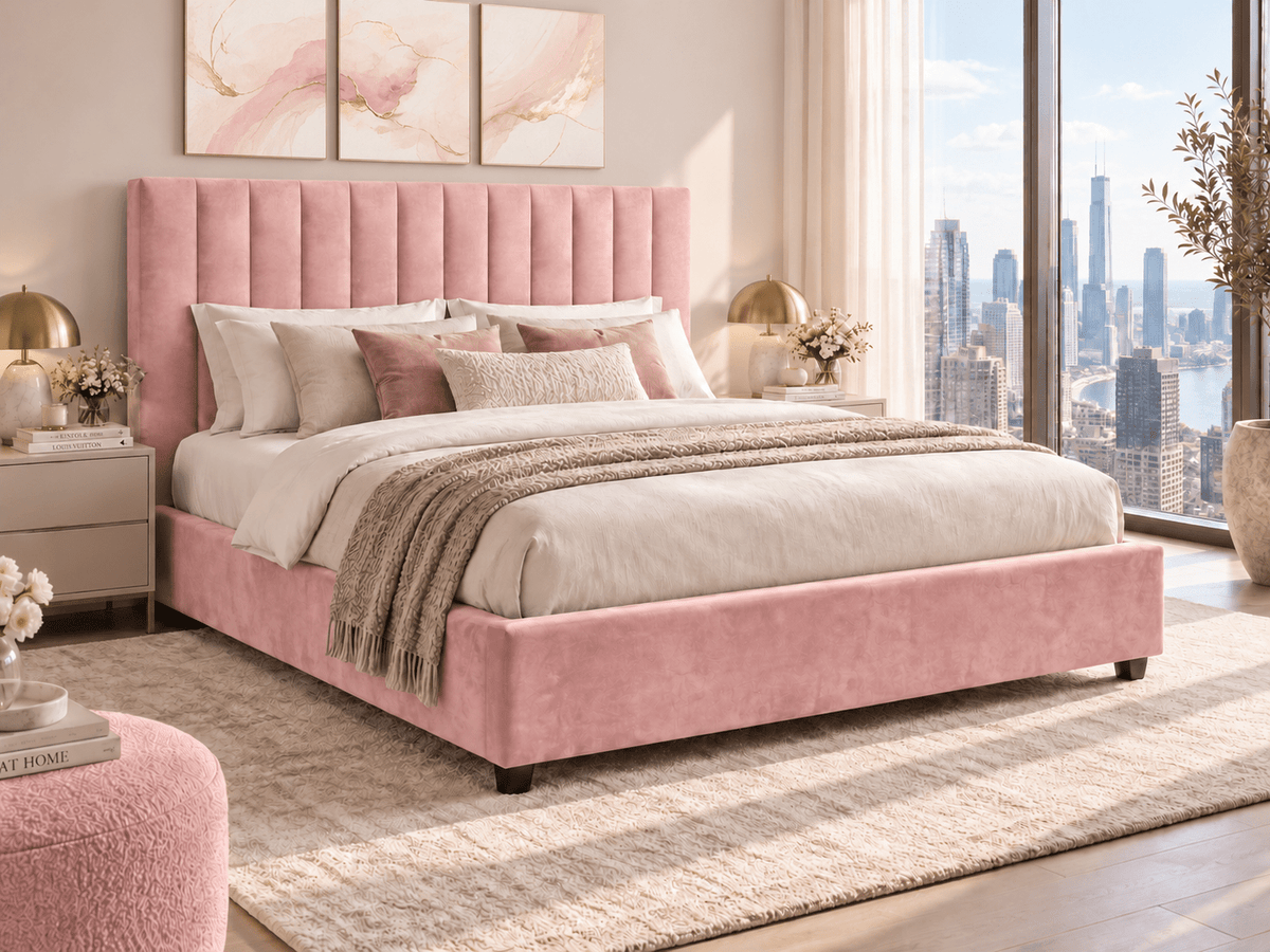 A pink upholstered bed with a tall tufted headboard and matching footboard, styled in a bright modern bedroom with white bedding, neutral pillows, a beige rug, and large windows overlooking a city skyline.