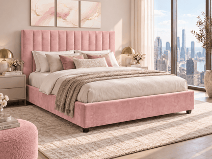 A pink upholstered bed with a tall tufted headboard and matching footboard, styled in a bright modern bedroom with white bedding, neutral pillows, a beige rug, and large windows overlooking a city skyline.
