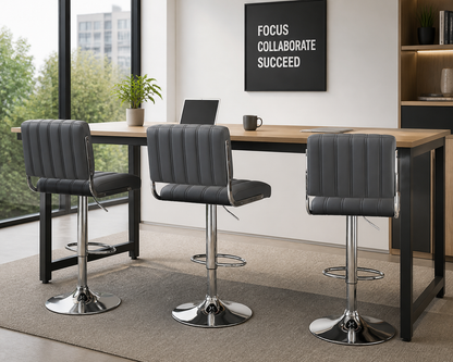 Three gray upholstered swivel bar stools with chrome pedestal bases arranged around a wooden-topped high table in a modern office setting.