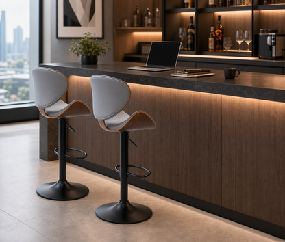 Two modern bar stools with light gray upholstered seats and curved brown wooden backs, set at a counter in a contemporary kitchen or bar interior with wood cabinetry and warm under-counter lighting.