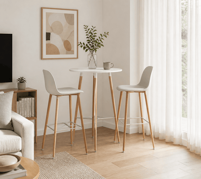 A small round white bar-height table with two light gray upholstered stools and natural wood legs, styled in a bright, modern living room corner.