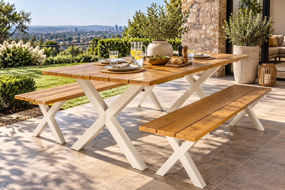 Outdoor dining set with a rectangular wooden table and two matching benches on a stone patio, set against a scenic garden background.