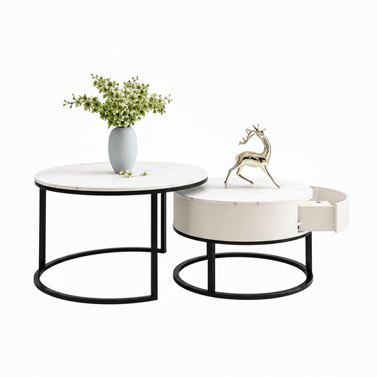 A modern nesting coffee table set, side table on the left and a matching round coffee table on the right with an open drawer. The tables have black metal circular frames and are styled with a light blue vase of green leaves and a gold deer figurine on a clean white background.