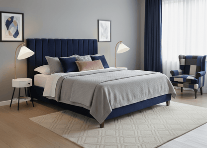 Modern bedroom with a blue upholstered bed, gray bedding, and decorative pillows. Featuring two white bed side tables and nightstand lamps