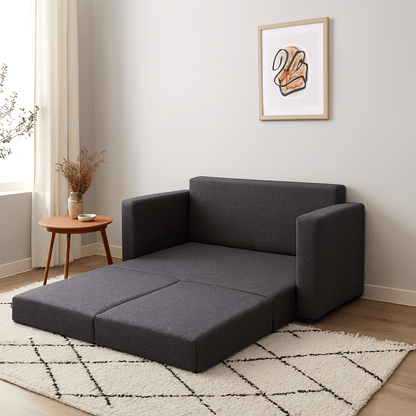 Grey opened sleeper sofa in a living room with a small table and artwork on the wall. That Couch Place